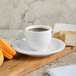 A white porcelain Villeroy & Boch saucer with a cup of coffee and macarons on a wooden board.