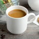 A Villeroy & Boch white porcelain mug filled with brown liquid on a saucer with a cookie and a spoon.