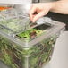 A hand using a Cambro clear sliding lid to cover a salad container of lettuce on a counter.