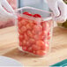 A gloved hand holding a plastic container of tomatoes.