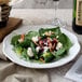 A Villeroy & Boch white porcelain plate with a vegetable salad and a glass of wine on a table.