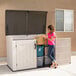 A woman in a pink shirt standing next to a Lifetime horizontal outdoor storage shed.