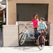 A woman and two children standing next to a Lifetime horizontal outdoor shed with a bicycle inside.