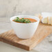 A Villeroy & Boch white porcelain gourmet bowl filled with soup on a cutting board.