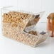 A clear stackable candy and topping dispenser filled with granola on a counter.