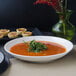 A Villeroy & Boch white porcelain deep bowl of soup with a sprig of green leaves.