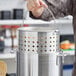 A person using a Winco aluminum stock pot steamer basket to cook on a stovetop.