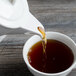 White porcelain teapot pouring tea into a cup.