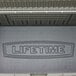 A black metal Lifetime outdoor storage box with rough cut textured metal surfaces and the Lifetime logo on the lid.