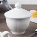 A Villeroy & Boch white porcelain covered sugar bowl with a spoon on a table.