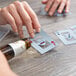 A hand pouring alcohol on a table with a person playing Hoyle cards.