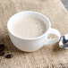 A white Villeroy & Boch porcelain cup of coffee with a spoon on a burlap surface.