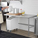 A man in a professional kitchen using a Regency stainless steel work table to hold large pots.