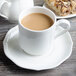 A white porcelain saucer with a cup of coffee and a pastry.