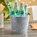 An American Metalcraft galvanized metal bucket filled with soda bottles on a table on an outdoor patio.