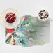 A table set with a cup of coffee and a Hoffmaster Holly Greetings Paper Placemat with holly leaves.