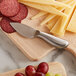 An American Metalcraft stainless steel cheese knife next to a cutting board with cheese and grapes.