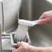 A hand holding a Carlisle Sparta Spectrum white brush with stiff bristles over a sink.