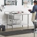 A woman standing in a kitchen with a Regency stainless steel work table with a sink on the counter.