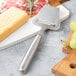 A Franmara stainless steel cheese plane next to a cheese board with cheese and grapes.