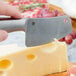 A person using an American Metalcraft stainless steel hard cheese cleaver to cut cheese on a counter.