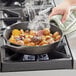 A person using a Choice pre-seasoned cast iron skillet to cook potatoes on a stove.