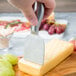 A hand using an American Metalcraft stainless steel hard cheese spade to cut cheese.