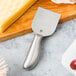 An American Metalcraft stainless steel hard cheese spade with a cheese on a cutting board.