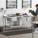 A man standing in a kitchen with a large stainless steel work table with a sink on the left.