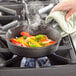 A Choice pre-seasoned cast iron skillet filled with cooking vegetables on a stovetop.