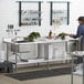 A man standing in a kitchen with a Regency stainless steel work table with a sink on the left.
