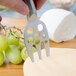 A person using a Franmara stainless steel fork to cut cheese.