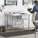 A woman standing in a professional kitchen with a Regency stainless steel work table with a sink on the counter.