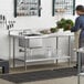 A man standing in a school kitchen using a Regency stainless steel work table with a sink on the counter to prepare vegetables.