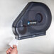 A hand pulling tissue paper from a black San Jamar toilet paper dispenser.