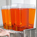 A person using a Crathco refrigerated beverage dispenser to pour orange juice into a glass.