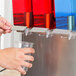 A person using a Crathco quadruple refrigerated beverage dispenser to fill a glass with red, blue, and green liquid.