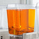 A white Crathco refrigerated beverage dispenser bowl filled with orange liquid.