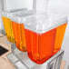 A Crathco triple plastic container with orange liquid.