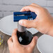 A person using a Franmara dark blue wine foil cutter to open a bottle of wine on a table.