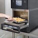 A person using a Merrychef eikon e2s Trend high-speed oven to cook french fries on a tray.