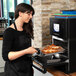 A woman wearing a black apron using a Merrychef eikon e2s countertop oven to cook food.