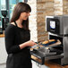 A woman wearing a black apron putting food into a Merrychef countertop oven on a kitchen counter.