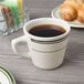 A Tuxton Green Bay tall china cup filled with coffee on a table with croissants.