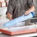 A person using a blue Vollrath Safety Mate Cooling Paddle in a clear container.