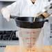 A woman in a white lab coat pouring liquid through a Matfer Bourgeat Exoglass bouillon strainer.