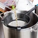 A chef using a Matfer Bourgeat Exoglass strainer to pour liquid into a pot.