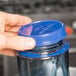 A hand holding a blue Tethered Cooling Paddle Cap on a plastic jar.
