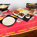 A Kansas City Chiefs plastic table cover on a table with bowls of food, chips, and a salad.