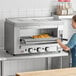 A woman using a Cooking Performance Group infrared salamander broiler to cook food in a professional kitchen.